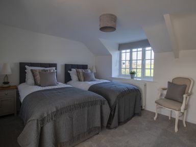 A bedroom with two single beds a window a bedside table with a lamp and a chair at Willowbrook Cottage Litton Cheney