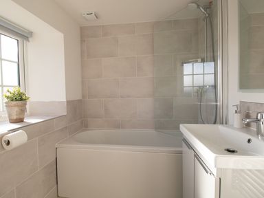 A bathroom with a bathtub shower and sink with a window and a plant at Willowbrook Cottage in Litton Cheney