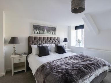 A bedroom with a large bed two bedside tables with lamps a window and a framed picture above the bed at Willowbrook Cottage in Litton Cheney