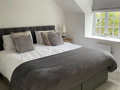 A bedroom with a double bed bedside table lamp and window with flowers at Willowbrook Cottage in Litton Cheney