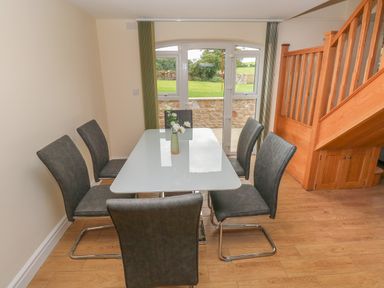 A dining area with a glass table surrounded by six chairs next to a wooden staircase and a window with a view outside at Woodpecker Barn in Hensol near Pontyclun