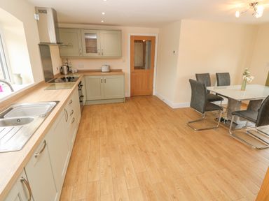 A kitchen with light wood flooring dining table with four chairs and green cabinets with appliances at Woodpecker Barn in Hensol near Pontyclun