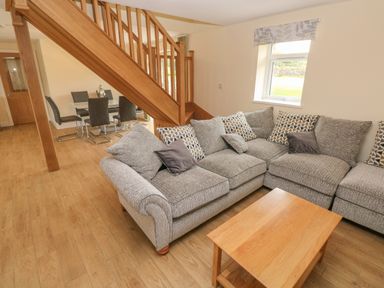 A living room with a gray sectional sofa and wooden coffee table below a staircase and a dining table with chairs at Woodpecker Barn in Hensol near Pontyclun