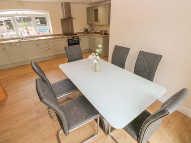 A kitchen and dining area with a white table and six gray chairs at Woodpecker Barn Hensol near Pontyclun
