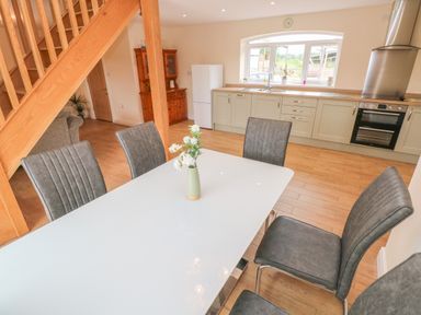A kitchen and dining area with a white dining table and grey chairs under wooden stairs at Woodpecker Barn in Hensol near Pontyclun