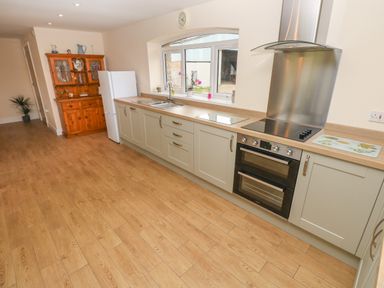 A kitchen with wooden floor, beige cabinets, white refrigerator, wooden cupboard, window, sink, stove, and oven at Woodpecker Barn in Hensol near Pontyclun
