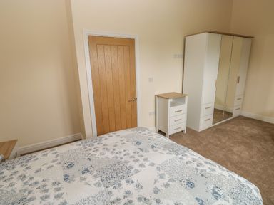 A bedroom with a wooden door a bed with patterned bedding a white nightstand and a white wardrobe with mirrored doors at Woodpecker Barn in Hensol near Pontyclun