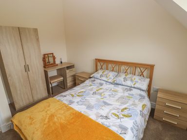 A bedroom with a double bed featuring patterned bedding a wooden wardrobe a desk with a small mirror and a chair and two wooden bedside tables at Woodpecker Barn in Hensol near Pontyclun
