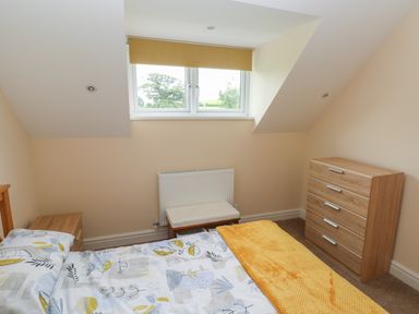 A bedroom with a bed a wooden chest of drawers and a window with a yellow blind at Woodpecker Barn in Hensol near Pontyclun