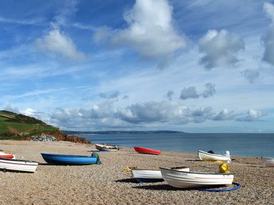 A pebble beach with small boats near the shore and a cliff in the background at The Reach in Hallsands