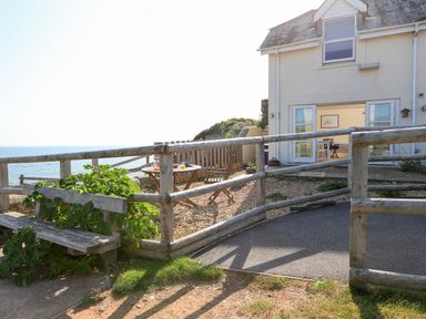 An outdoor seating area with wooden chairs and table near a house with open doors overlooking the sea at The Reach in Hallsands