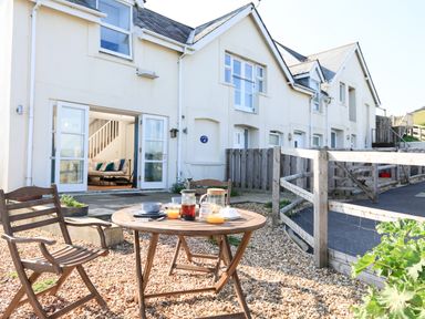 A patio area with a round wooden table and two wooden chairs outside a row of white houses at The Reach in Hallsands
