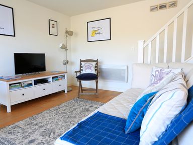 A living room with a sofa a chair a TV on a stand and framed pictures on the wall at The Reach in Hallsands