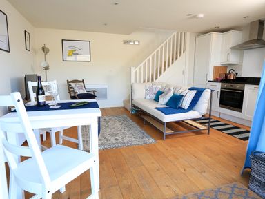A living room with a white dining table and chairs a sofa with cushions and a kitchen area at The Reach in Hallsands