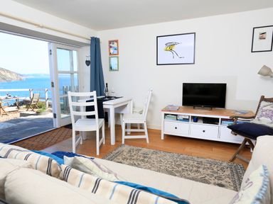 A living area with a small dining table and chairs a TV on a stand and a view of the sea at The Reach in Hallsands