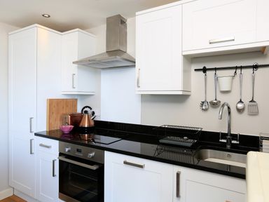A kitchen with white cabinets black countertop electric stove oven stainless steel sink and hanging utensils at The Reach in Hallsands