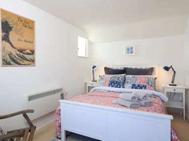 A bedroom with a white bed with patterned bedspread and pillows two bedside tables with lamps and folded towels on the bed at The Reach in Hallsands