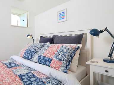A bedroom with a white bed frame patchwork bedding two blue lamps on bedside tables and a small window at The Reach in Hallsands