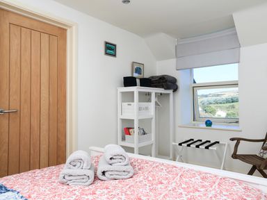 A bedroom with a bed, rolled towels, a wooden door, shelving unit, window with a view, and a chair at The Reach in Hallsands