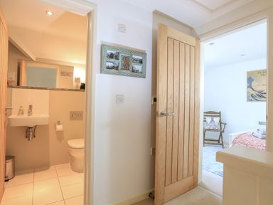 A hallway showing a bathroom with a sink and toilet and a bedroom with a chair and bed at The Reach in Hallsands