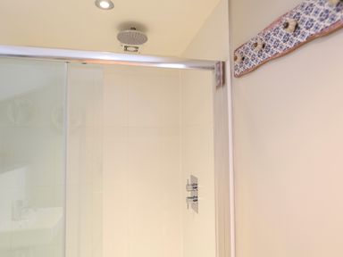 A shower area with glass sliding door and chrome showerhead with controls on tiled wall at The Reach in Hallsands