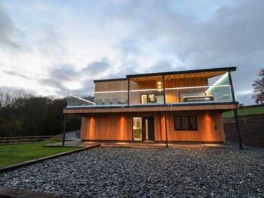 A modern two-story wooden house with glass balcony and outdoor lights at Fron Haul - Robin Goch in Llanfwrog near Ruthin