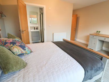 A bedroom with a bed pillows and a desk near wooden doors at Fron Haul - Robin Goch Llanfwrog near Ruthin