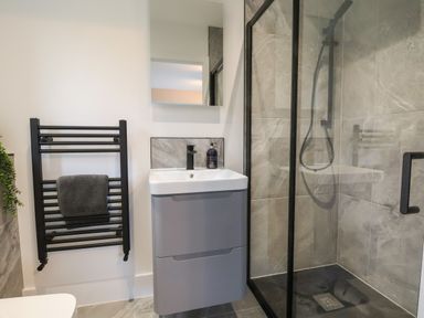A bathroom with a sink vanity mirror towel rack and a glass-enclosed shower at Fron Haul - Robin Goch in Llanfwrog near Ruthin
