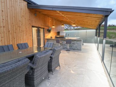An outdoor covered patio with dining table and chairs a bar counter with stools and a hot tub at Fron Haul - Robin Goch in Llanfwrog near Ruthin