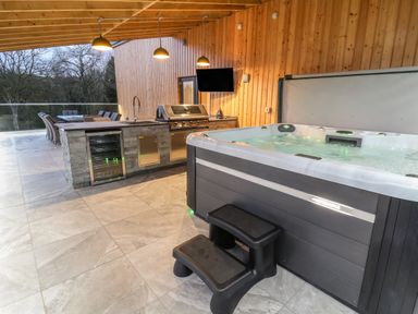 An outdoor patio area with a hot tub, kitchen island with grill, sink, and wine fridge at Fron Haul - Robin Goch in Llanfwrog near Ruthin