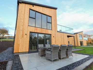 A wooden exterior house with a patio table and chairs on a tiled area at Fron Haul - Robin Goch in Llanfwrog near Ruthin