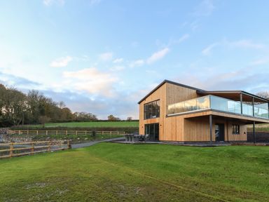 A modern wooden house with large windows and a balcony in a grassy countryside setting at Fron Haul - Robin Goch in Llanfwrog near Ruthin