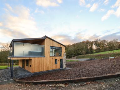 A two story wooden house with a balcony in a rural area at Fron Haul - Robin Goch in Llanfwrog near Ruthin