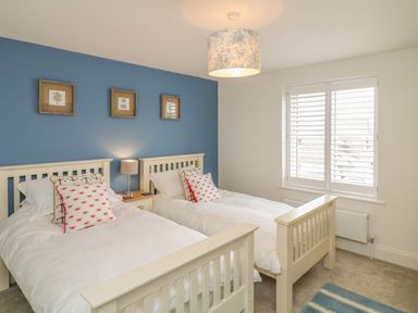 A bedroom with two single beds with white bedding and pillows in front of a blue wall with three framed pictures at Beacon House in St Agnes