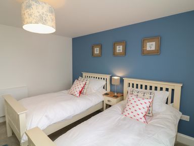 A bedroom with two single beds a bedside table and a lamp with blue accent wall at Beacon House in St Agnes
