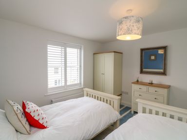 A bedroom with two single beds a wardrobe a chest of drawers and a window at Beacon House in St Agnes