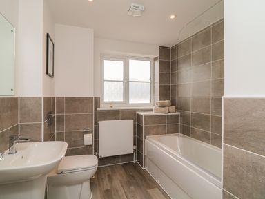 A bathroom with a bathtub towels on a shelf a toilet a sink and a window at Beacon House in St Agnes