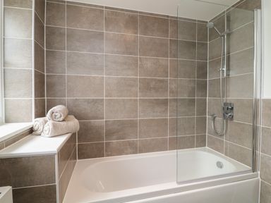 A bathroom with a bathtub shower combination and rolled towels on the ledge at Beacon House in St Agnes