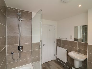 A bathroom with a shower, white door, radiator, sink, and mirror at Beacon House in St Agnes