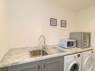 A utility room with a sink microwave mini fridge washing machine and dryer at Beacon House in St Agnes