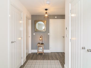 A hallway with white doors a small wooden table with a lamp and a round mirror on a gray wall at Beacon House in St Agnes