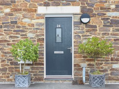A front door with the number 24 flanked by two potted plants on a stone wall at Beacon House in St Agnes