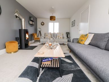 A living room with gray and yellow furniture a coffee table a black stove and a rug at Beacon House in St Agnes