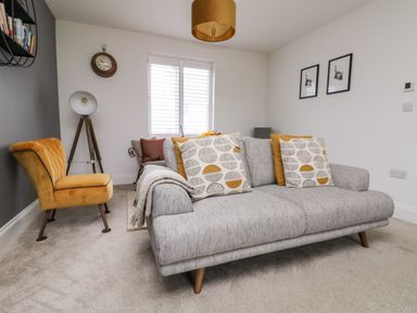 A living room with a gray sofa with patterned cushions a yellow chair a tripod lamp a wall clock and two framed pictures at Beacon House in St Agnes