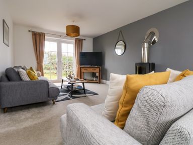 A living room with two sofas yellow and white cushions coffee table and television near glass doors at Beacon House in St Agnes