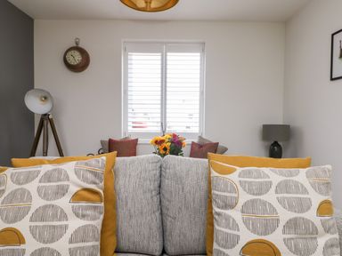 A living room with patterned cushions on a sofa a floor lamp a wall clock and flowers on a table at Beacon House in St Agnes