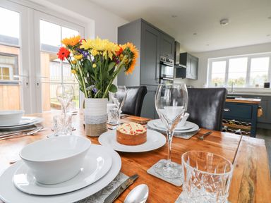 A dining table set with white dishes glasses and a vase of flowers in a kitchen at Beacon House in St Agnes