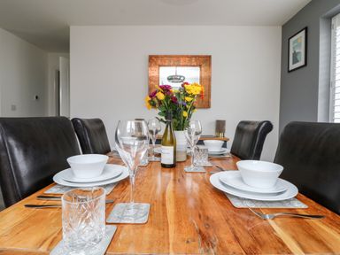 A dining table set with white dishes glasses and cutlery with flowers and a wine bottle at Beacon House in St Agnes