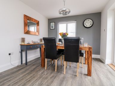 A dining room with a wooden table four black chairs a vase with flowers and a side table with a mirror at Beacon House in St Agnes