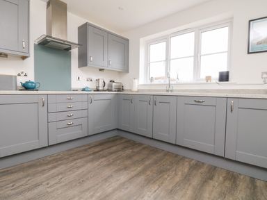 A kitchen with grey cabinets wooden floor and large windows at Beacon House in St Agnes